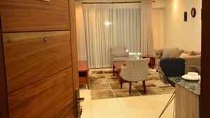 A room with a wooden door labeled '206', a dining table with chairs, a sofa, and a small kitchen area with a marble countertop. - Yohana Residences (Nairobi)