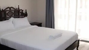 A neatly made bed with white linens, a wooden headboard, and a small bedside table. - Yohana Residences (Nairobi)