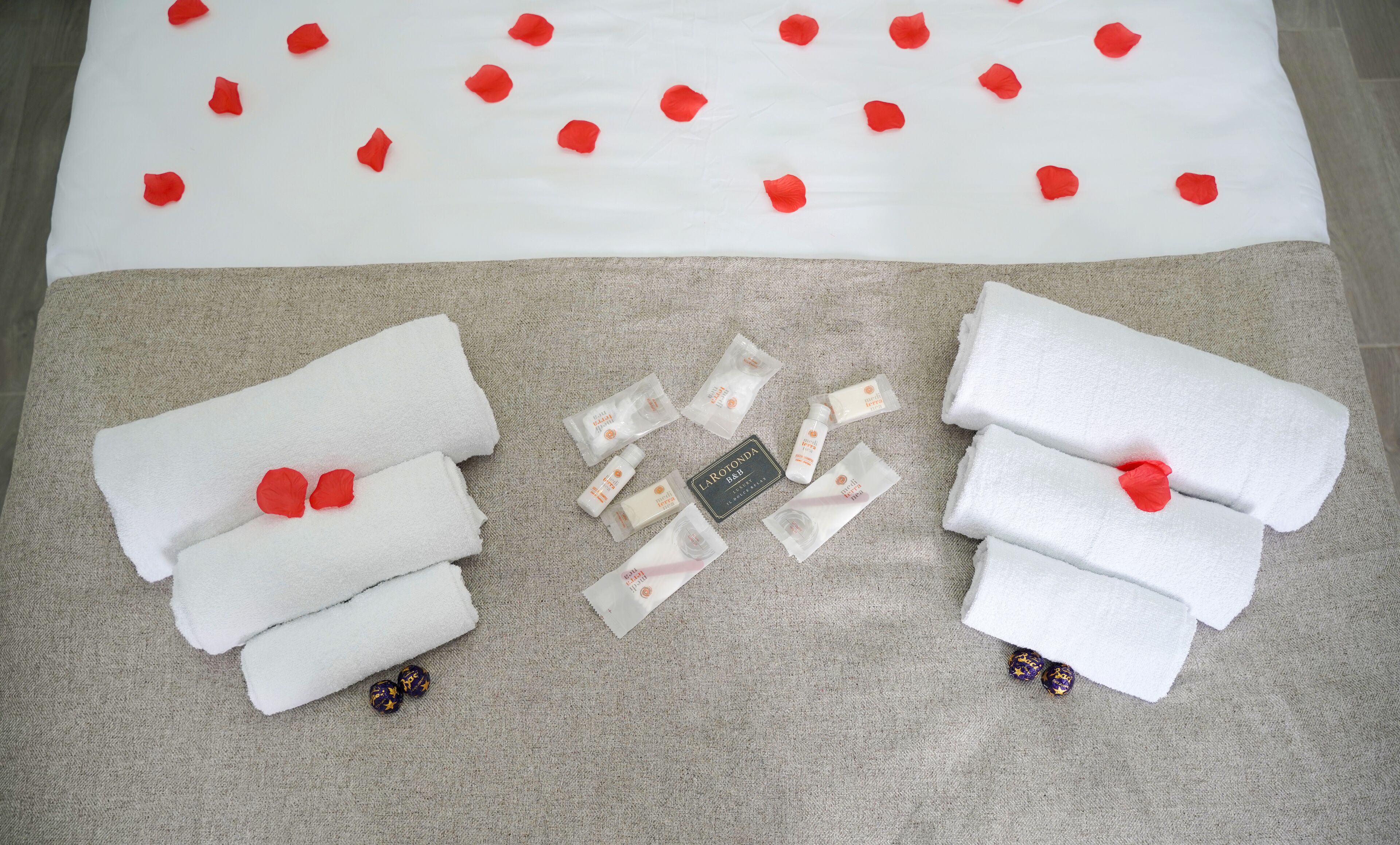 Toallas blancas ordenadas, artículos de aseo y pétalos de rosa decorativos sobre un piso alfombrado.