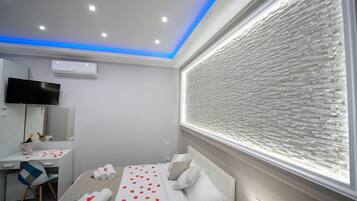 Une chambre d’hôtel moderne équipée d’un lit, d’un bureau, d’une télévision et d’une grande fenêtre donnant sur un mur à texture.