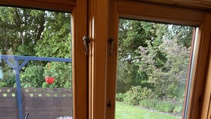 Una ventana con marco de madera que da a un jardín, una mesa con sillas y dos botellas de vidrio vacías en el alféizar.