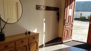 Una habitación con un armario de madera, un espejo redondo, una puerta que da al exterior y un piso de baldosas.