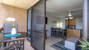 Eine moderne Wohnung mit einer Schiebetür zu einem Balkon, einem Essbereich mit Küche im Hintergrund und einer kleinen Sitzecke mit Teppich.