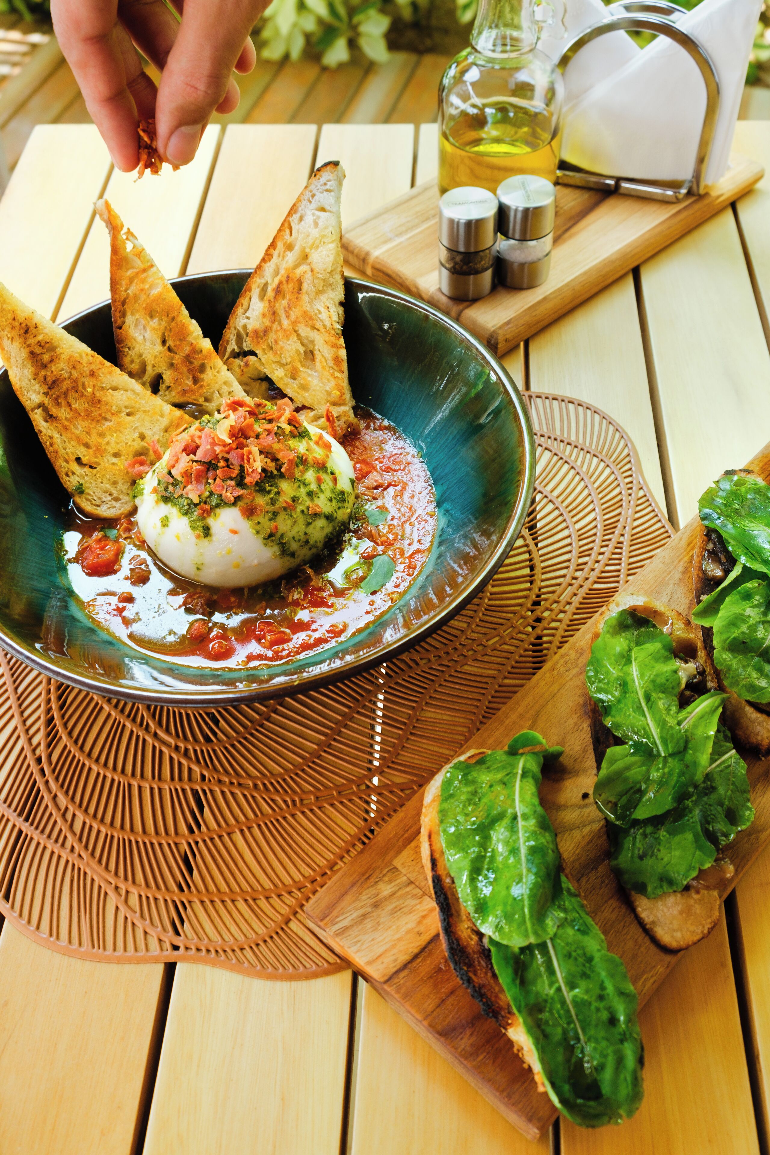 A bowl of food with bread and a bottle of oil on a wooden table.