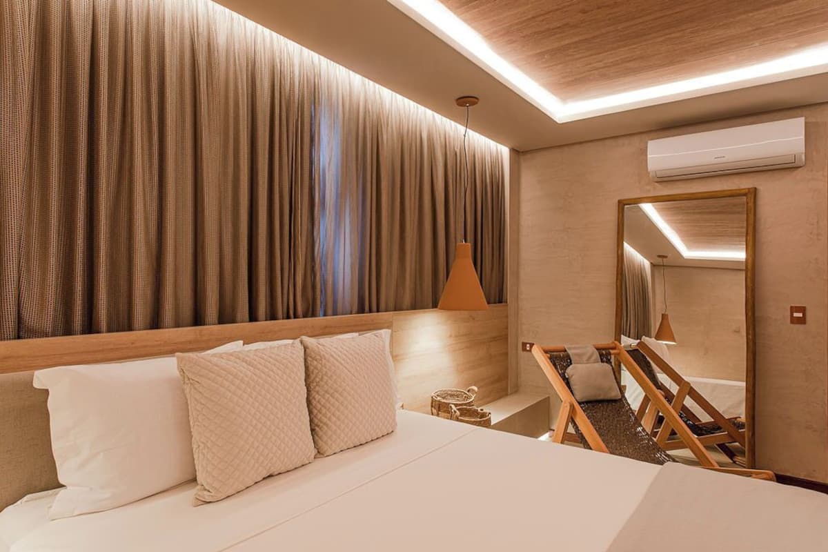Ein Hotelzimmer mit einem großen Bett, einem Holzkopfende, einer Wand-Klimaanlage, einer Deckenleuchte und einem Spiegel.