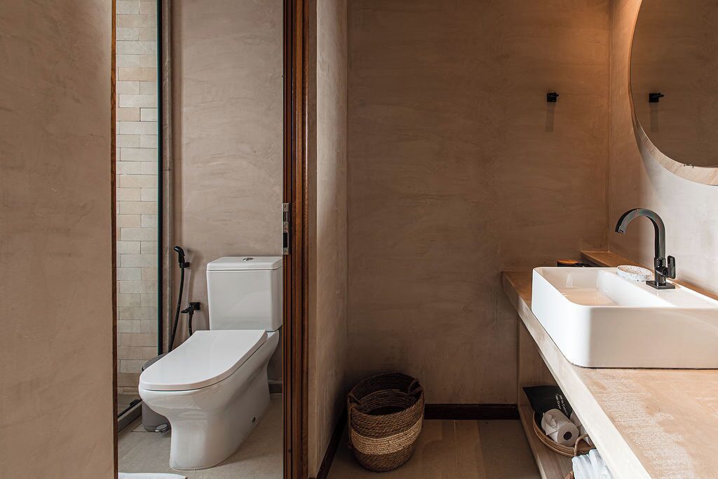A modern bathroom with a toilet, sink, and a small basket on the floor.