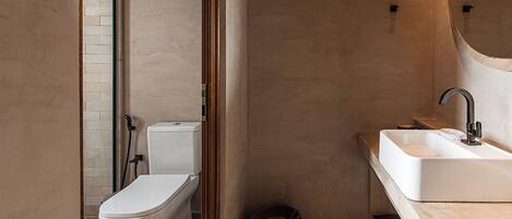 A modern bathroom with a toilet, sink, and a small basket on the floor.