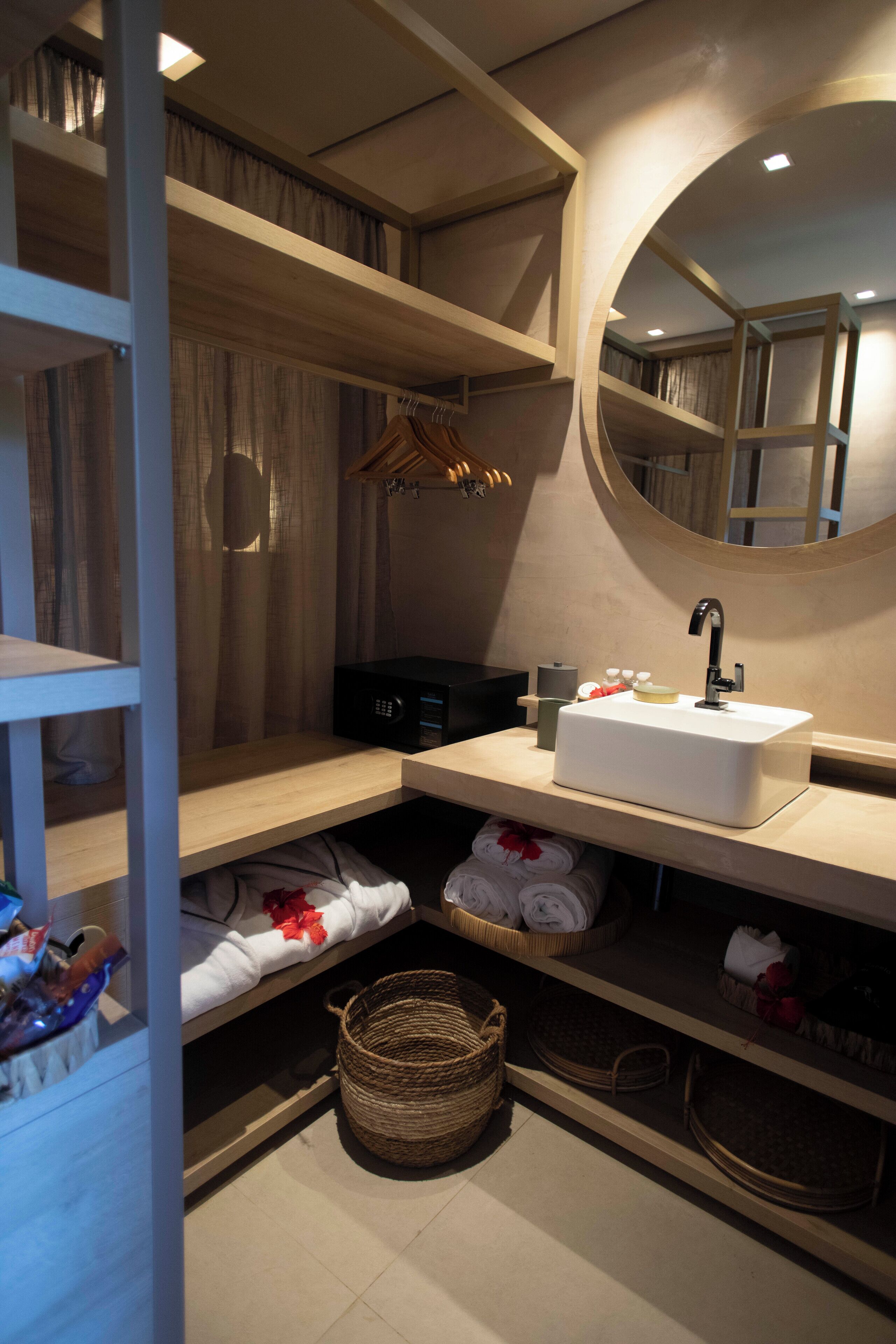 A modern bathroom with a white sink, wooden shelves, a mirror, and a hanging towel rack.