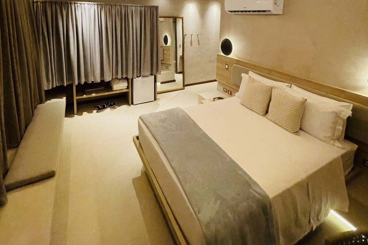 Ein modernes Hotelzimmer mit einem großen Bett, einem Schminktisch mit Spiegel, einer Klimaanlage und einer Decke mit eingelassenen Leuchten.