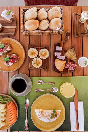 A wooden table with various food items, including bread rolls, cheese, and a plate with a slice of pizza. - POUSADA DO MIRANTE (Fernando de Noronha)