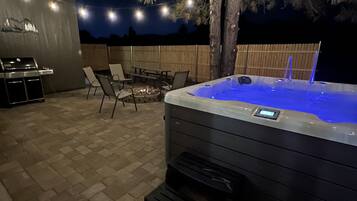 An outdoor patio area with a hot tub, a barbecue grill, and outdoor seating.