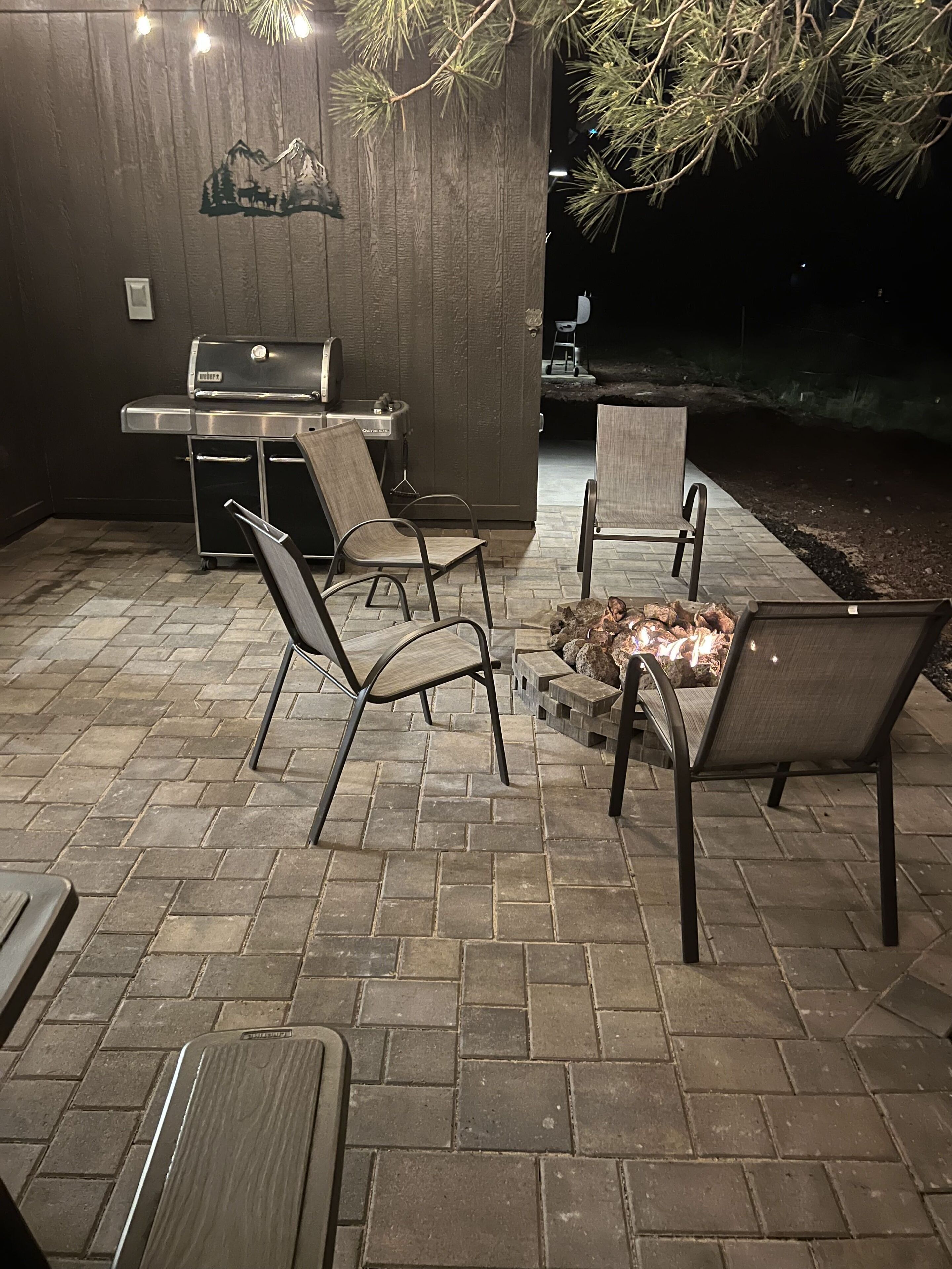 Un patio exterior con suelo de ladrillo, sillas de metal, una parrilla y una chimenea.