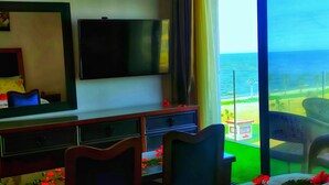 Een hotelkamer met een grote televisie, een bed, een bureau en een balkon met uitzicht op zee.