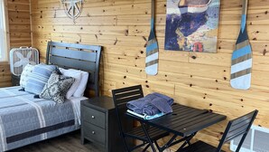 Um quarto acolhedor estilo cabana, com uma cama, uma mesa e duas cadeiras. Há um quadro na parede e dois remo de madeira pendurados.