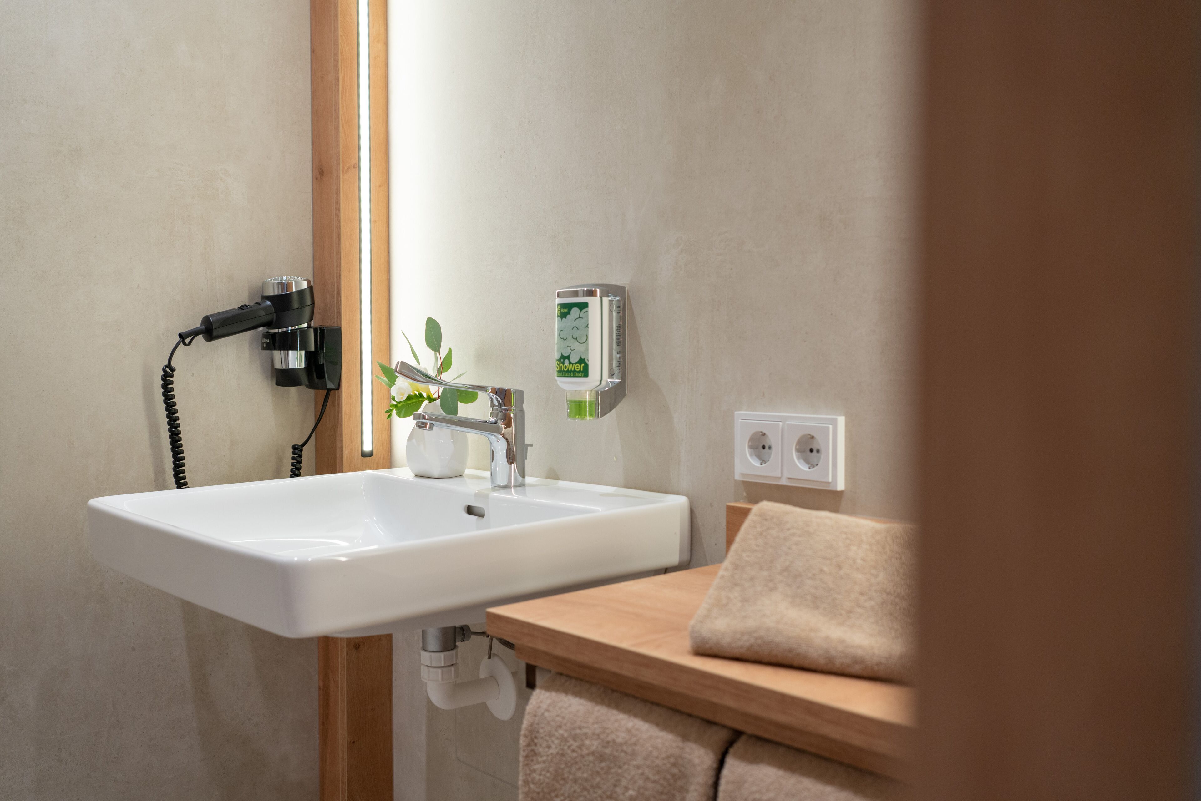 Un baño con lavamanos blanco, toallero, planta y panel de control de ducha.