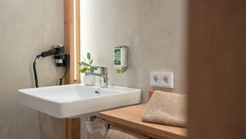 Un baño con lavamanos blanco, toallero, planta y panel de control de ducha.