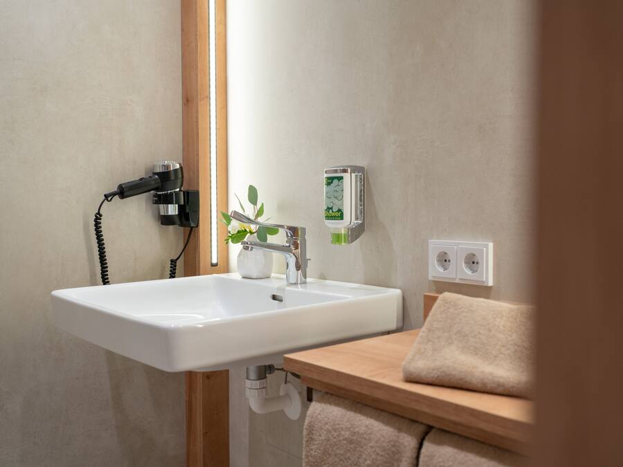 Un baño con lavamanos blanco, toallero, planta y panel de control de ducha.