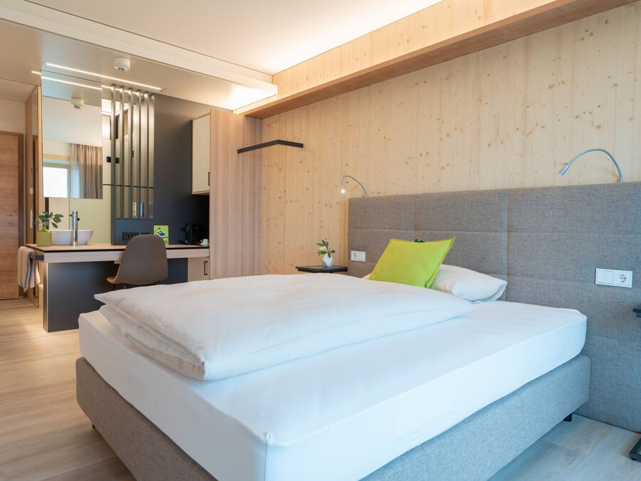 A modern hotel room with a large bed, a desk, and a chair.