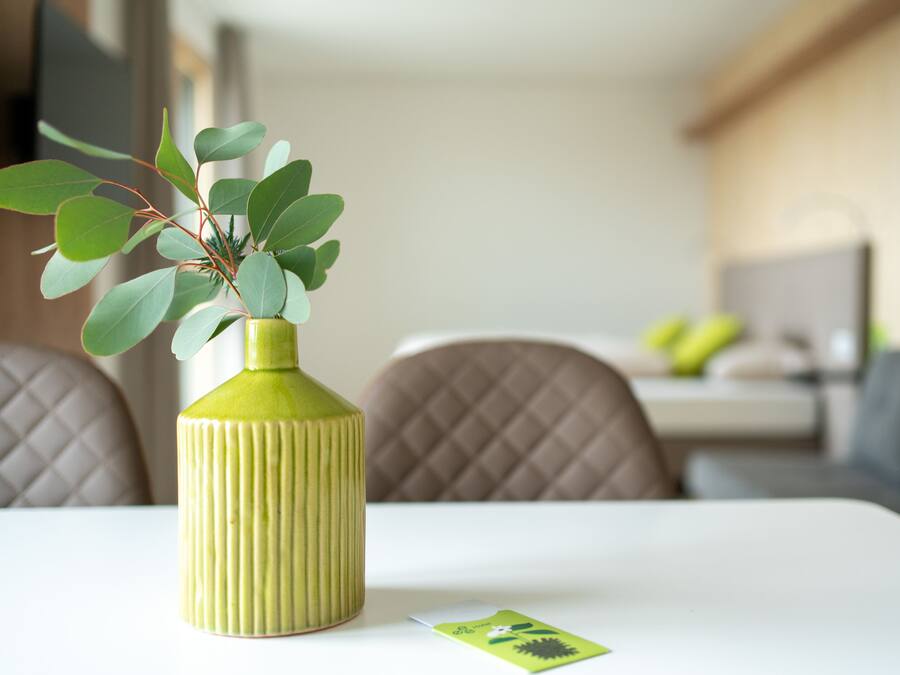 Un jarrón verde con hojas sobre una mesa blanca en una habitación moderna con un sofá y comedor.