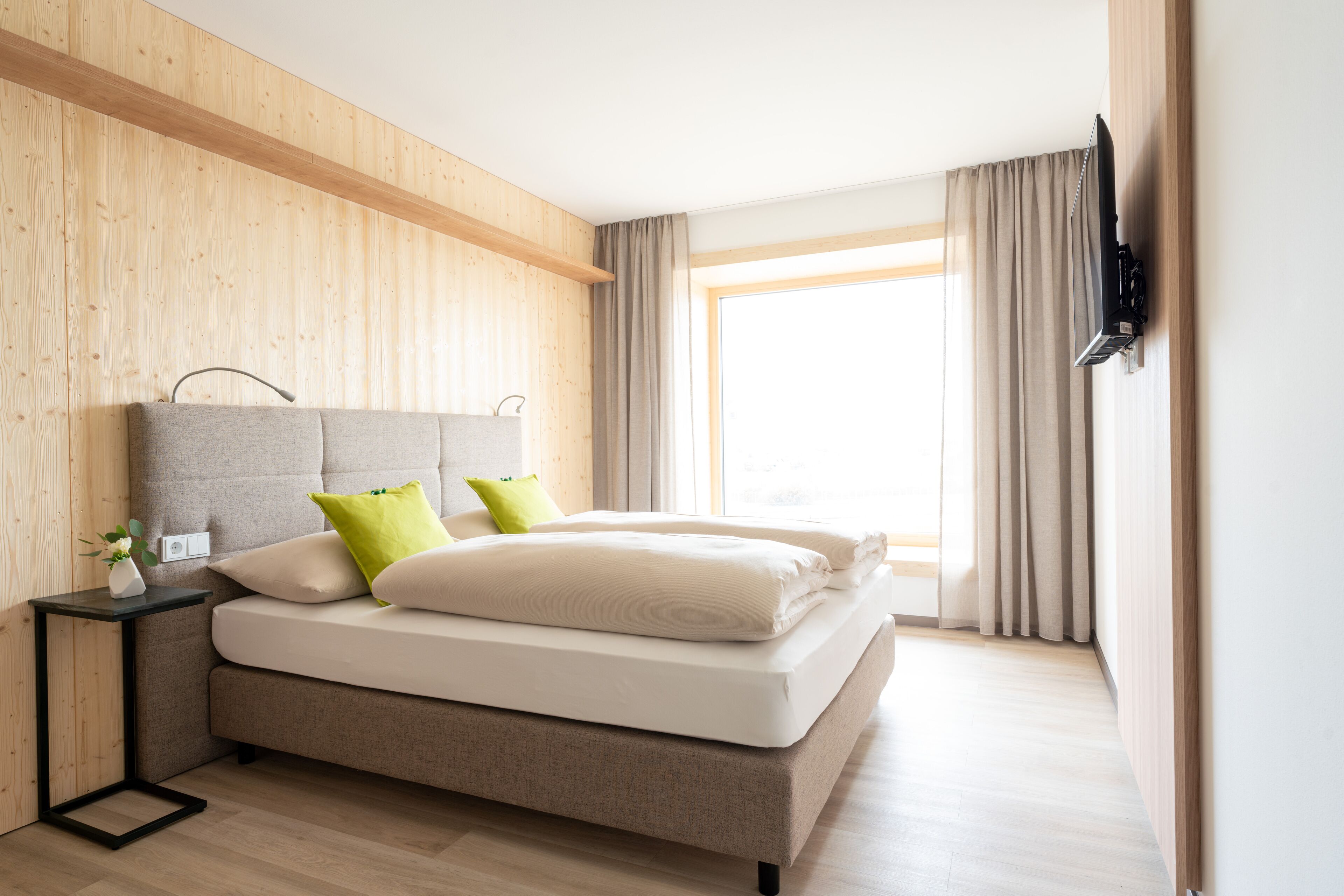 Un dormitorio moderno con una cama grande, una mesita de noche y un televisor montado en la pared.
