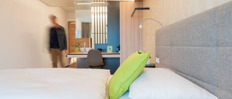 Quarto de hotel moderno com cama, escrivaninha e banheiro.