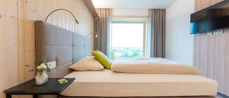 Un dormitorio moderno con una cama grande, una mesita de noche con un florero y un televisor de pantalla plana montado en la pared.