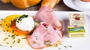 Ein Frühstückstisch mit Brot, Schinken, Käse und einer Tasse Kaffee.
