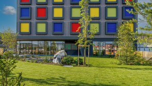 Un hotel moderno con fachada colorida, césped cuidado y una escultura de roca.