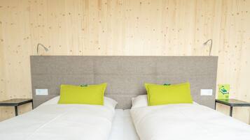 A double bed with white bedding and two bright green pillows, a grey headboard, and two bedside tables with lamps.
