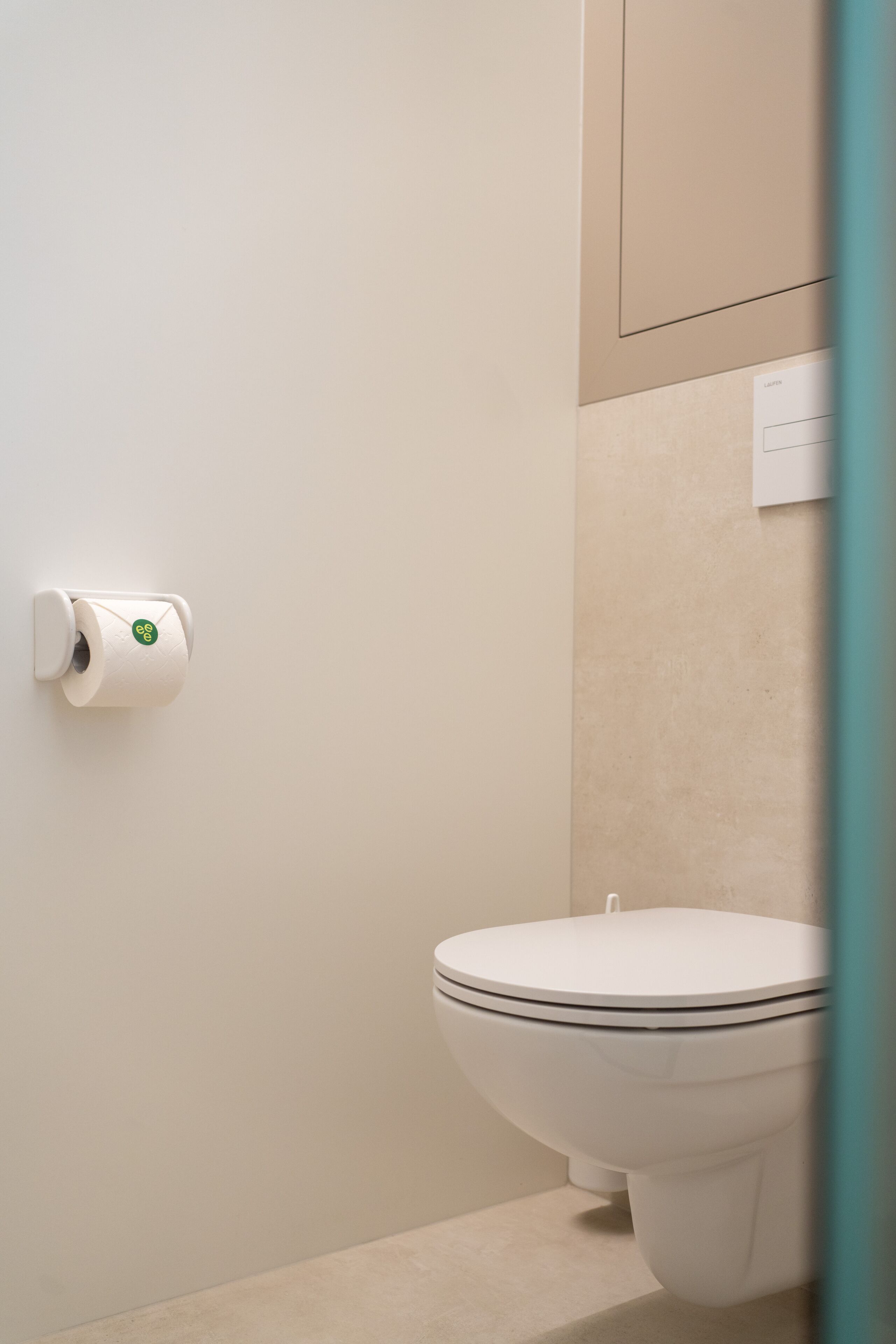 Een toilet met een witte spoelknop en een toiletpapierhouder aan de muur.