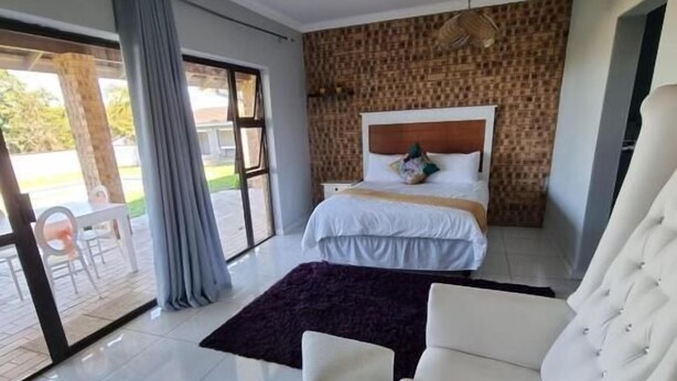 A modern bedroom with a large bed, a white armchair, and a view through a glass door to an outdoor area. - Leading Guest Farm  (Margate)