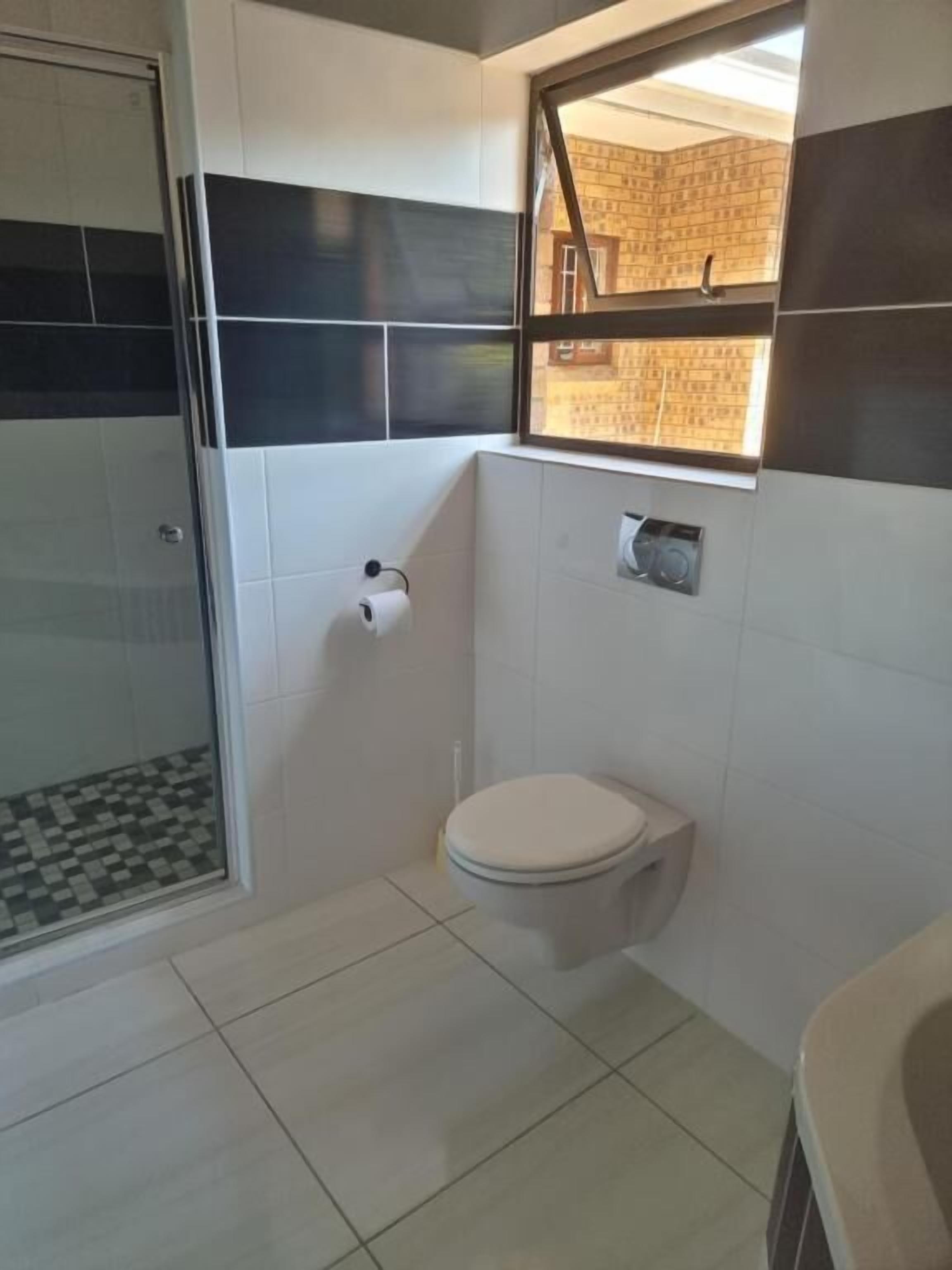 A bathroom with a toilet, a shower, and a window with a view of a brick wall.