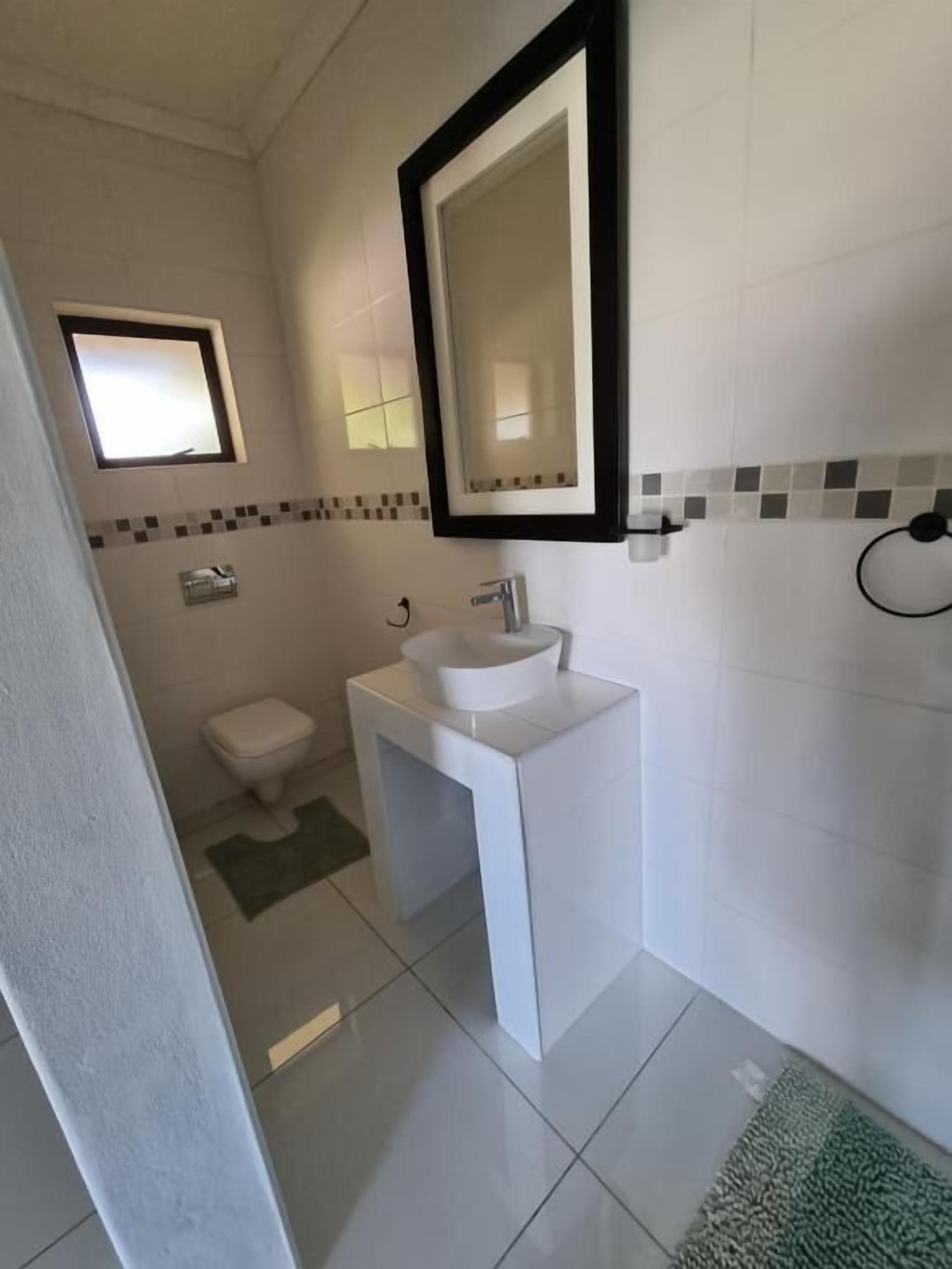 Un baño con un lavamanos blanco, un espejo, un inodoro y una pequeña ventana.