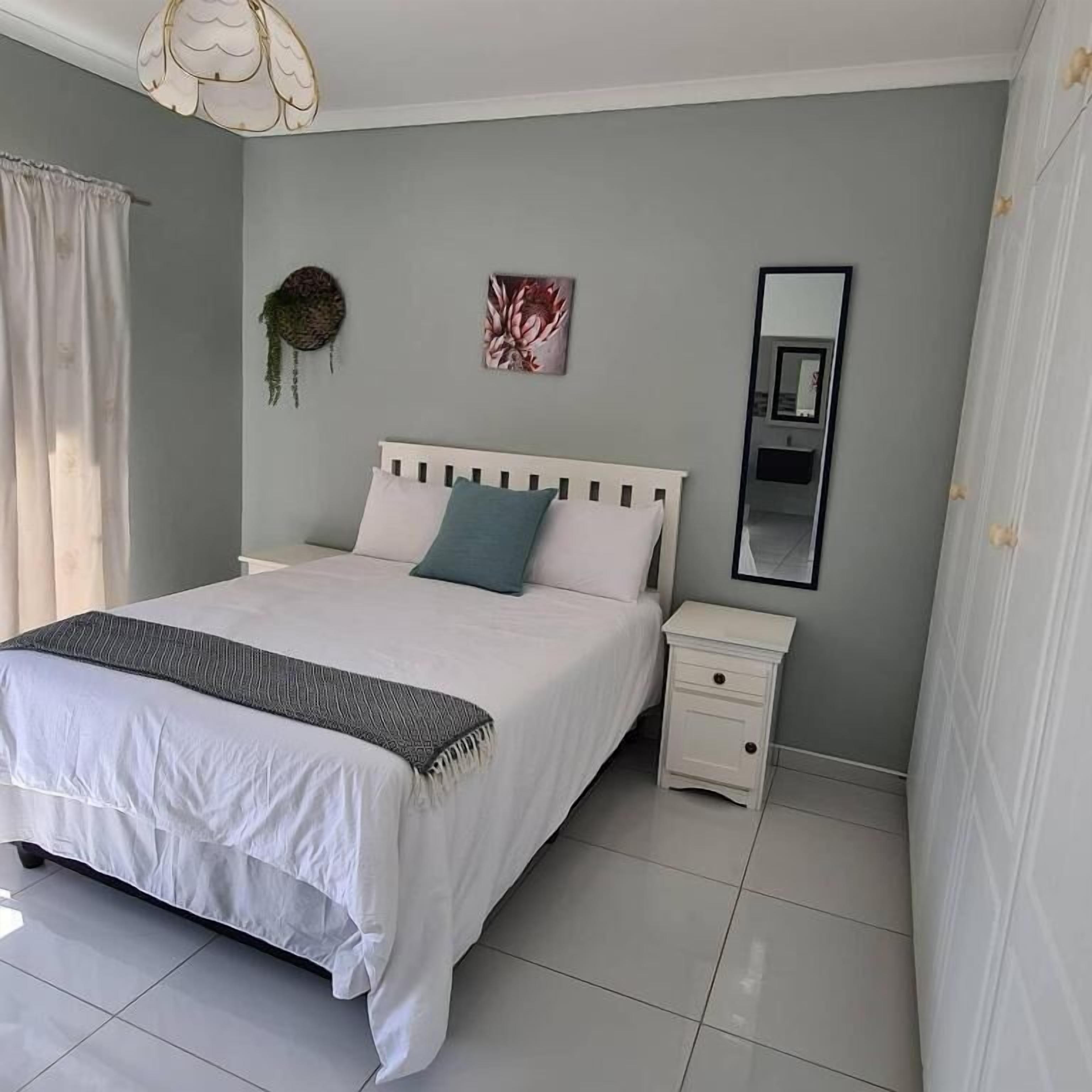 A bedroom with a bed, a nightstand, a mirror, and a wall-mounted artwork.