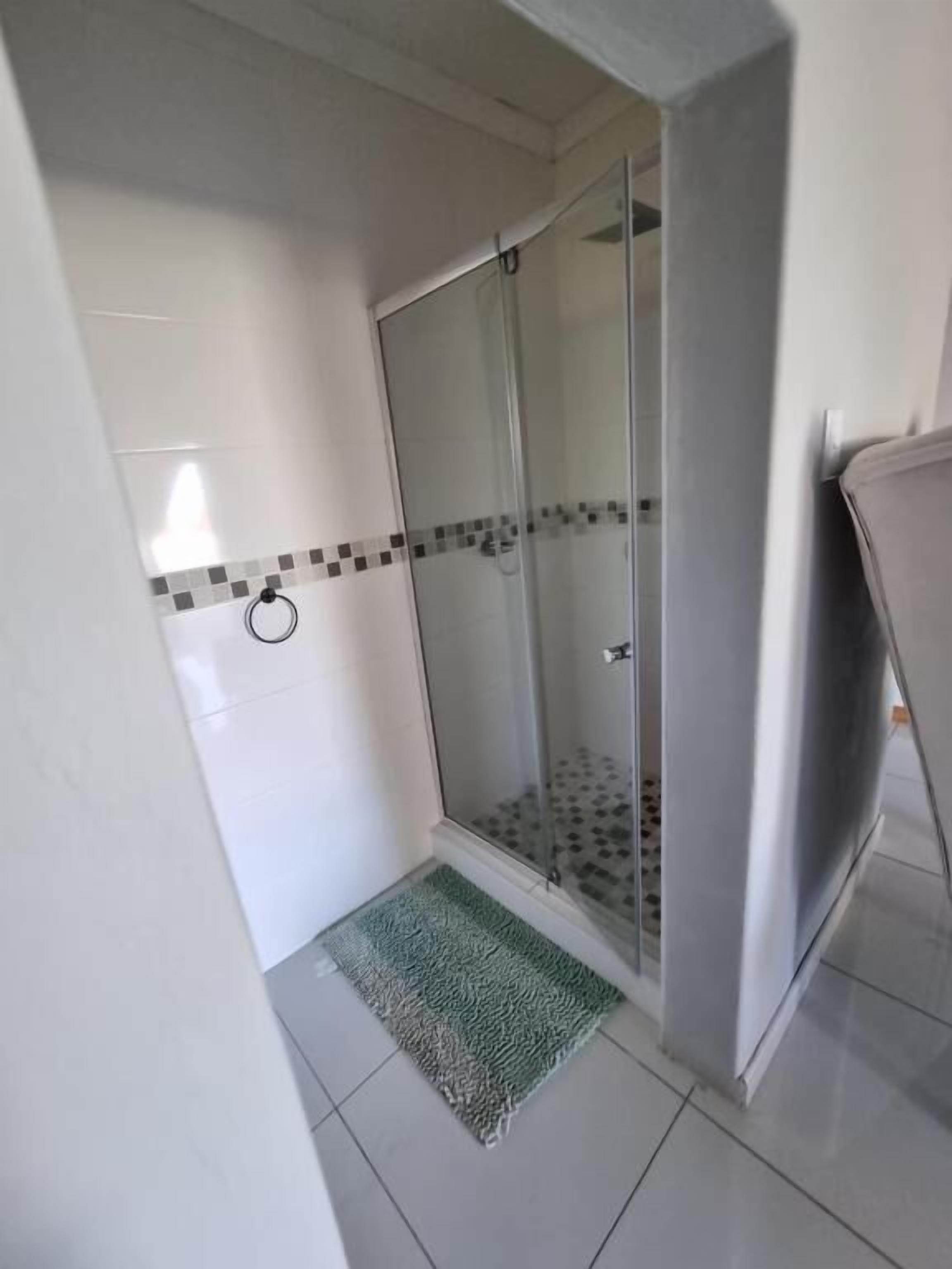 A small, enclosed shower area with a glass door, a tiled floor, and a green mat.