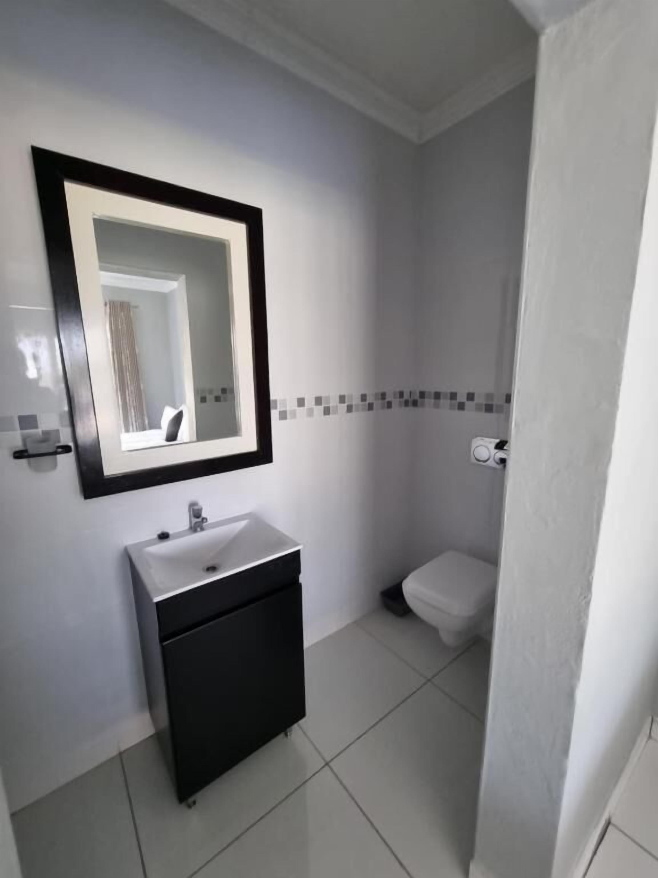 A modern bathroom with a white sink, black cabinet, and a mirror with a black frame.