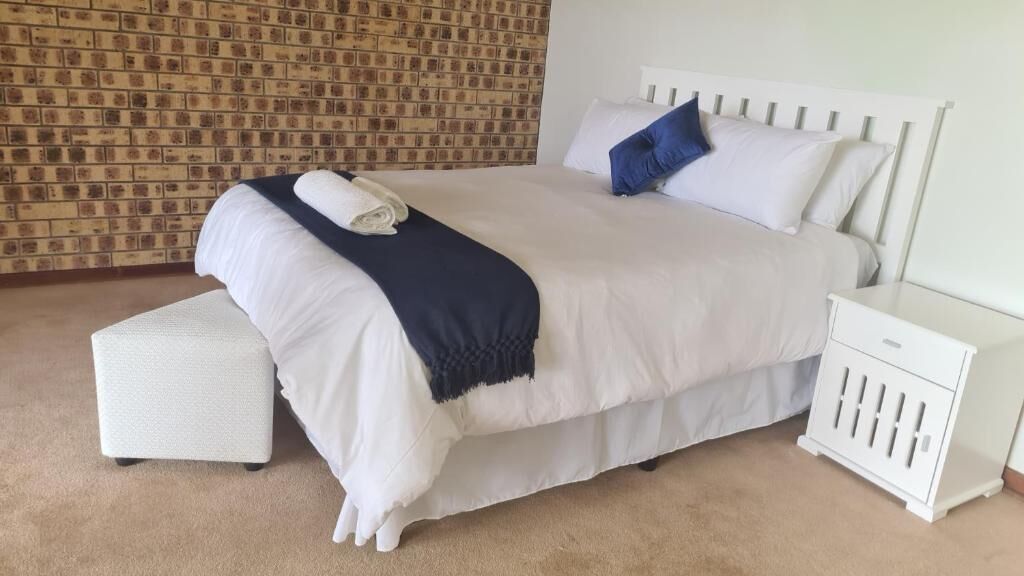 A neatly made bed with a white headboard, a matching bedside table, and a small white bench.