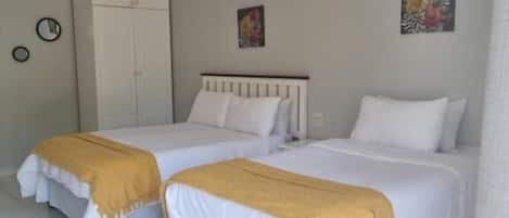 A hotel room with two beds, a wardrobe, and two wall-mounted paintings.