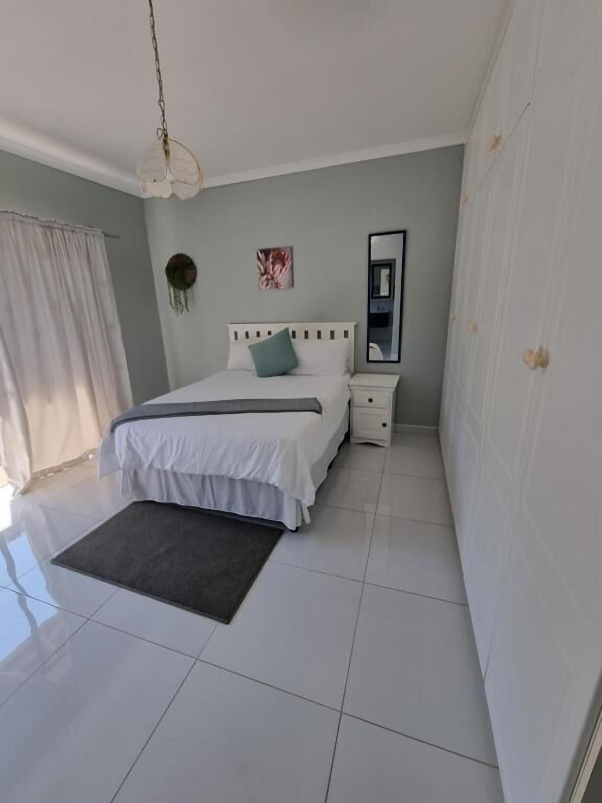 Un dormitorio con cama, mesita de noche, espejo y lámpara colgante.