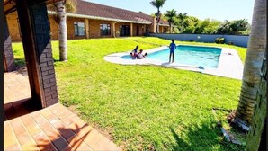 A backyard with a swimming pool, a covered patio, and a house in the background. - Leading Guest Farm  (Margate)