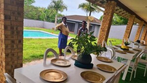 An outdoor dining area with tables set for a meal, surrounded by chairs and a pool in the background. - Leading Guest Farm  (Margate)