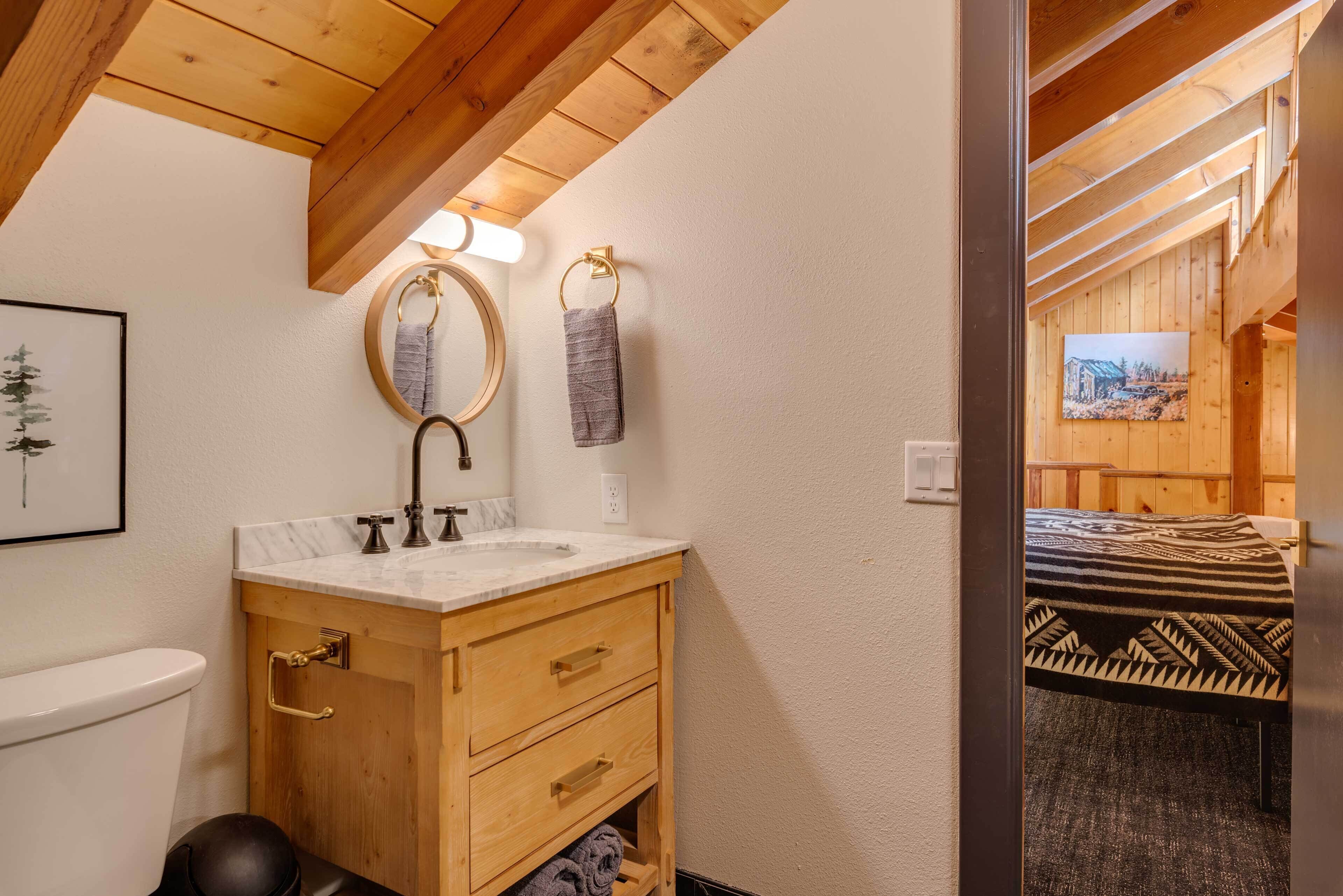 A wooden cabin bathroom with a wooden vanity, a sink, and a toilet. There is a framed picture on the wall and a towel hanging on a hook.