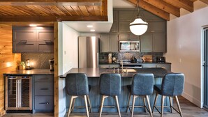 A modern kitchen with a central island, bar stools, and a hanging light fixture.
