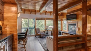 A wooden cabin interior with a kitchen, dining area, and large windows.