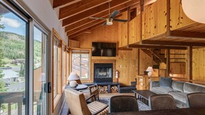 A cozy cabin interior with a fireplace, wooden walls, and a large window overlooking a scenic landscape.