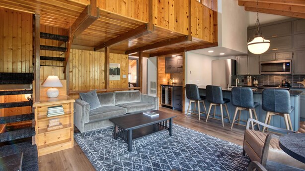 A modern interior with a wooden staircase, a sofa, a coffee table, and a kitchen area with bar stools.