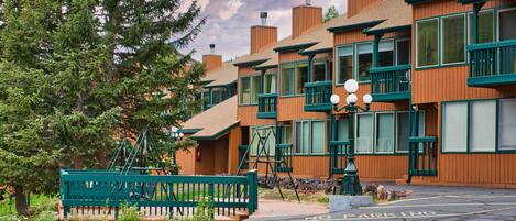 A row of wooden buildings with green accents, a bench, and a 'No Parking' sign.