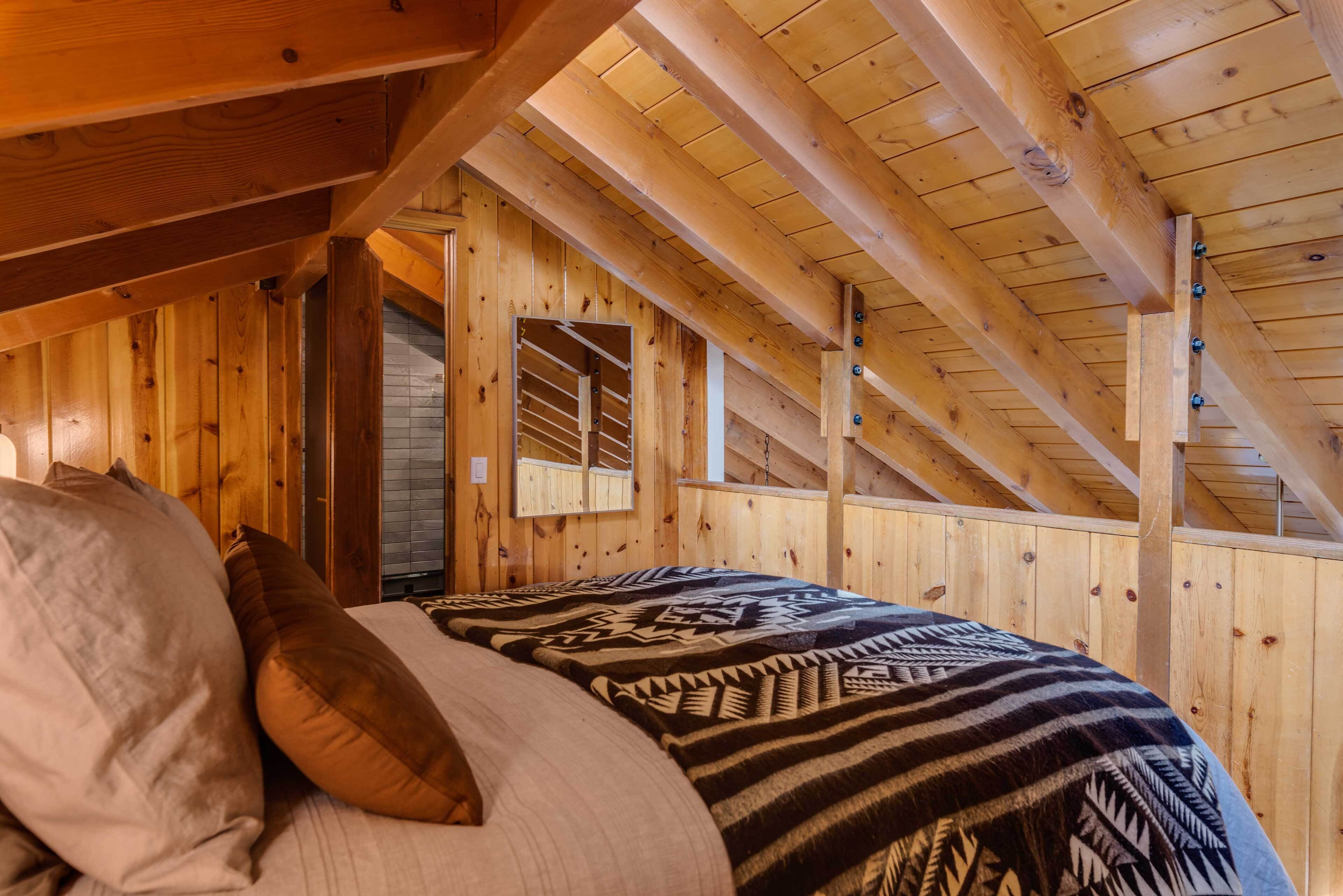 Un intérieur en bois avec un lit, des oreillers et une couverture à motifs.