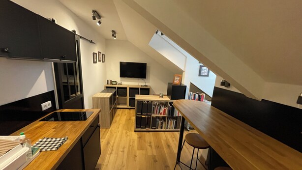 A modern kitchen with wooden countertops, a built-in oven, and a dining area with a high table and bar stools. - Studio MODERNE (Barcelonnette)