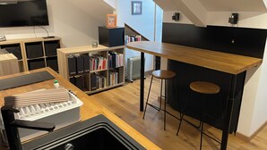 A modern kitchen with a wooden countertop, black bar stools, and a built-in bookshelf. - Studio MODERNE (Barcelonnette)